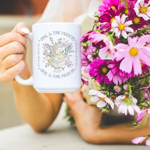Puede incluir: Taza de cer&aacute;mica blanca con un dise&ntilde;o floral y el texto "OPAL & JUNE MOCKUPS." La taza est&aacute; siendo sostenida por una mano.