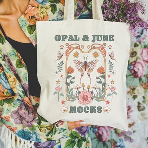Può includere: Borsa tote color crema con un design floreale e a farfalle. La borsa presenta il testo "OPAL & JUNE MOCKS" in un font retrò. Il design include farfalle, fiori e funghi nei toni dell'arancione, del rosa e del verde.