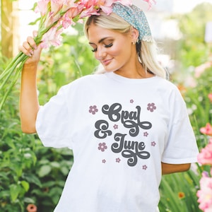 May include: White t-shirt with a graphic design that says "Opal & June" in a retro font with pink flowers surrounding the text.
