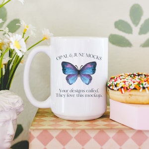 Pu&ograve; includere: Tazza in ceramica bianca con un motivo a farfalla blu e il testo "OPAL & JUNE MOCKS Your designs called. They love this mockup."