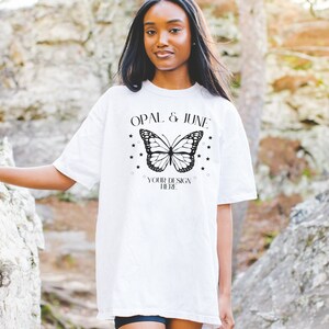 K&ouml;nnte beinhalten: Wei&szlig;es Oversize-T-Shirt mit einem schwarzen Schmetterlingsmotiv und dem Text "Opal & June" und "Your Design Here" auf der Vorderseite.