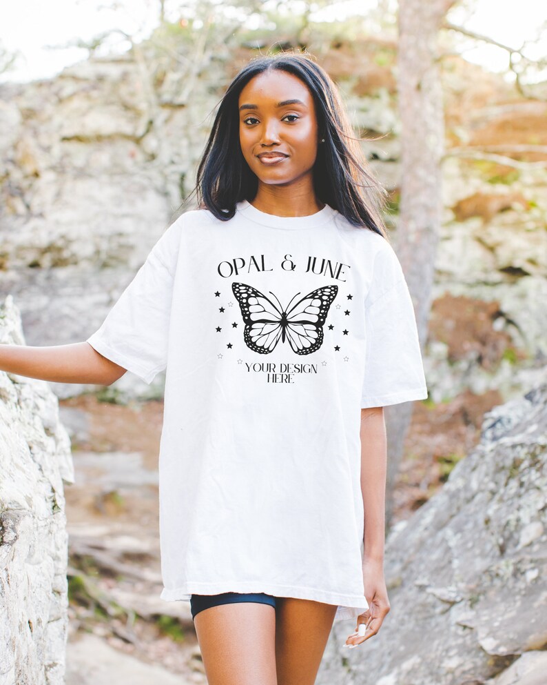 K&ouml;nnte beinhalten: Wei&szlig;es Oversize-T-Shirt mit einem schwarzen Schmetterlingsmotiv und dem Text "Opal & June" und "Your Design Here" auf der Vorderseite.