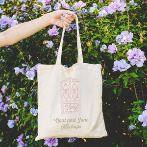 May include: A white canvas tote bag with a pink and white floral design of a vintage armoire. The bag has the text "Opal and June Mockups" printed on the front.