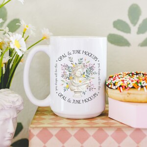 Pu&ograve; includere: Una tazza in ceramica bianca con un design floreale e il testo "OPAL & JUNE MOCKUPS. your designs will love this * OPAL & JUNE MOCKUPS" stampato su di essa.