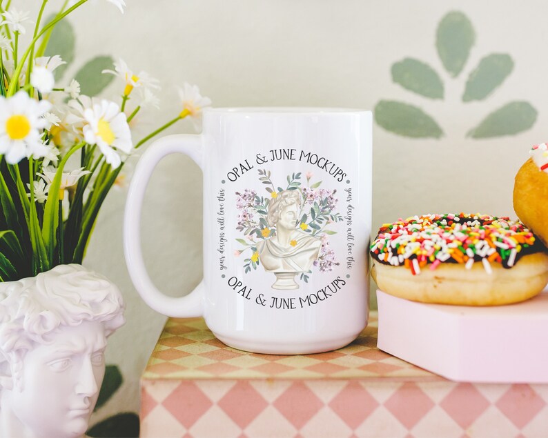 Pu&ograve; includere: Una tazza in ceramica bianca con un design floreale e il testo "OPAL & JUNE MOCKUPS. your designs will love this * OPAL & JUNE MOCKUPS" stampato su di essa.
