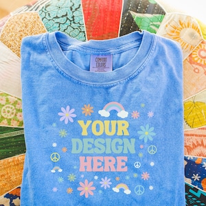 Photograph of Periwinkle Comfort Colors® Tee: Folded Shirt Mockup of Blue T-Shirt Lying on Boho Cushion | Colorful Mock for Print on Demand