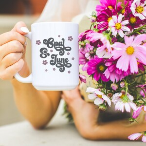 Puede incluir: Taza de cer&aacute;mica blanca con un dise&ntilde;o en blanco y negro que dice "Opal & June" con flores rosas alrededor del texto.