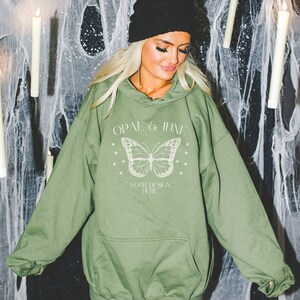 May include: A green hooded sweatshirt with a white butterfly graphic and the text "OPAL & JUNE" and "YOUR DESIGN HERE".