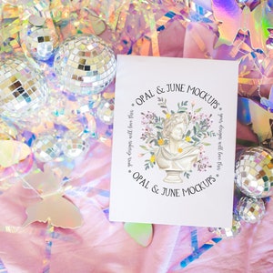 K&ouml;nnte beinhalten: Eine wei&szlig;e Karte mit dem Text "OPAL & JUNE MOCKUPS" in schwarzer Schrift. Die Karte ist umgeben von schillernden Schmetterlingen, Discokugeln und rosa Seidenpapier.