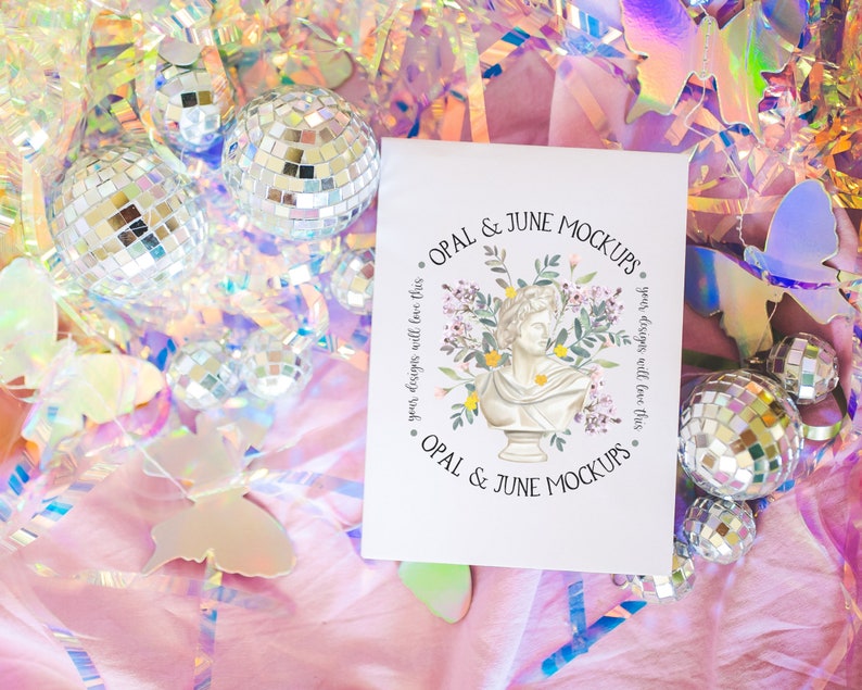 K&ouml;nnte beinhalten: Eine wei&szlig;e Karte mit dem Text "OPAL & JUNE MOCKUPS" in schwarzer Schrift. Die Karte ist umgeben von schillernden Schmetterlingen, Discokugeln und rosa Seidenpapier.