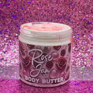 May include: A white jar with a pink lid and a pink and white label. The label says "Guided Rose Jam Type Body Butter". The jar is filled with a white cream.