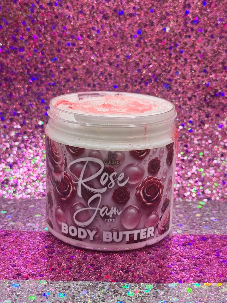 May include: A white jar with a pink lid and a pink and white label. The label says "Guided Rose Jam Type Body Butter". The jar is filled with a white cream.