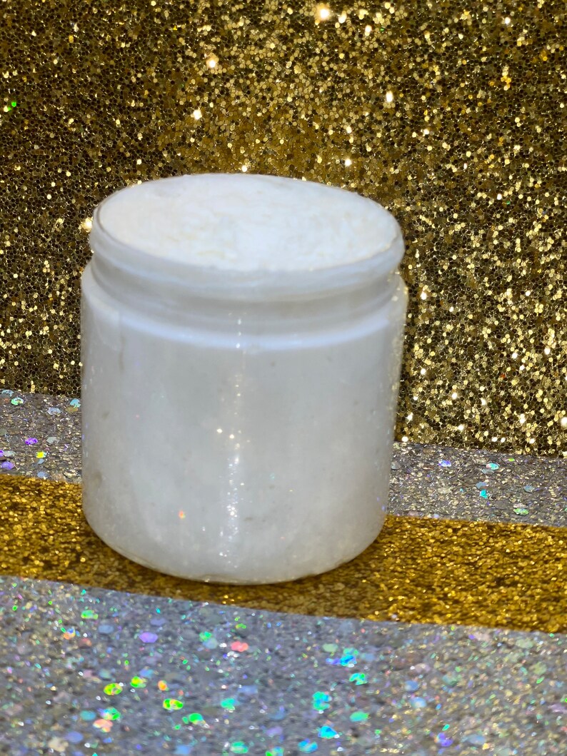 May include: A white jar filled with a white, creamy substance. The jar is sitting on a gold and silver glitter surface.