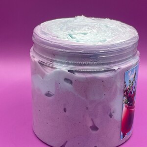 May include: A clear jar filled with a light purple and light blue whipped body butter. The jar has a label with a floral design.