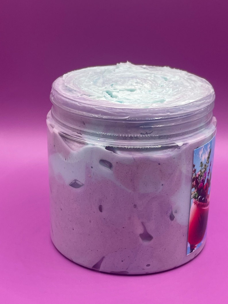 May include: A clear jar filled with a light purple and light blue whipped body butter. The jar has a label with a floral design.
