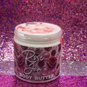 May include: A white jar with a pink lid and a pink and white label. The label says "Rose Jam Type Body Butter" and has a pink rose design.
