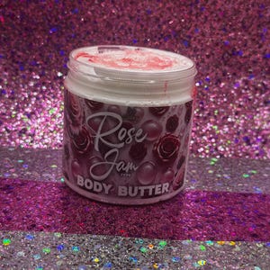 May include: A white jar with a pink lid and a pink and white label that says "Rose Jam Type Body Butter". The jar is sitting on a pink and white glittery surface.