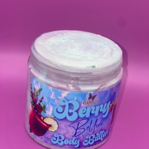 May include: A white jar of Gummy Berry Bellini Body Butter with a blue and white swirl on top. The jar has a colorful label with a butterfly logo, a glass of berry drink, and the text "Gummy Berry Bellini Body Butter".