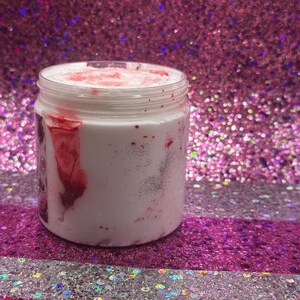May include: A white jar with a red and white swirl design. The jar is filled with a white substance and has a red lid.