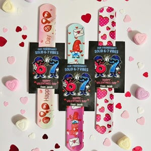 May include: An assortment of Valentine's Day-themed bookmarks and candies. The bookmarks feature various designs, including hearts, balloons, and a gnome, with the text "Happy Valentine's Day" and "Our Friendship? Solid 6-7 Vibes". Heart-shaped candies are scattered around.