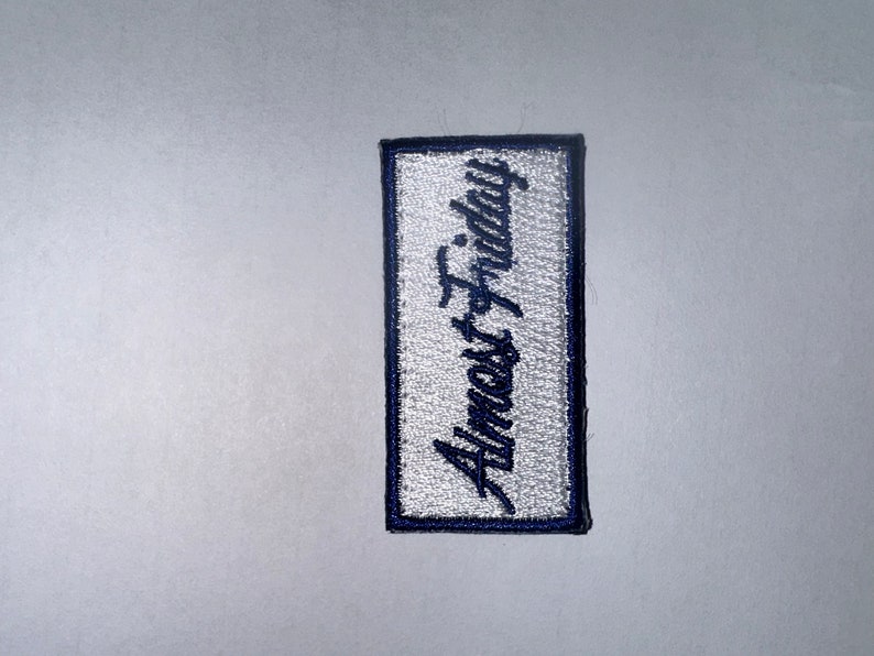 May include: White embroidered patch with blue stitching, featuring the text "Almost Friday" in a cursive font.