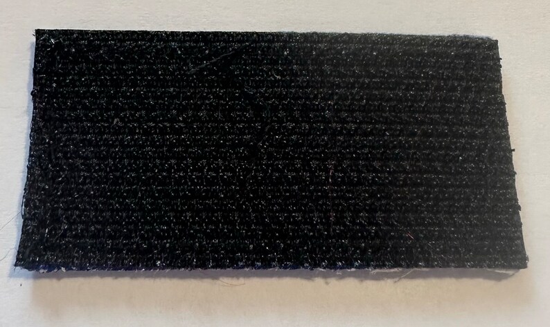 May include: A black hook and loop fastener, also known as Velcro, with a textured surface.