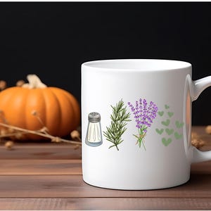 May include: A white ceramic mug featuring a printed graphic of a silver salt shaker, a sprig of green rosemary, a bundle of purple lavender, and several small green hearts arranged in a horizontal row on the front surface of the mug.