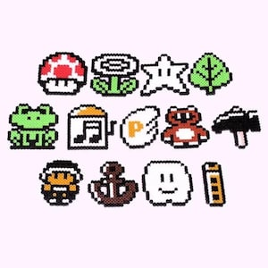 May include: A set of 13 pixel art character charms, including a green frog, a red mushroom, a brown bear, a white star, a green leaf, a brown anchor, a white ghost, a yellow hammer, a brown music note, a white P, a white face, a yellow ladder, and a brown flower.