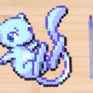 May include: A blue and purple perler bead cat with a white belly and a sad expression. The cat is sitting on a wooden surface.