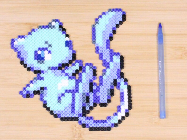 May include: A blue and purple perler bead cat with a white belly and a sad expression. The cat is sitting on a wooden surface.