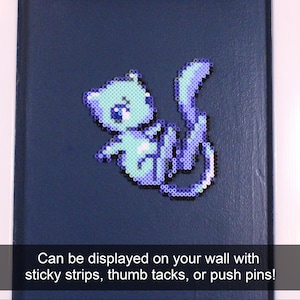 May include: A light blue and purple pixel art cat on a dark blue background. The cat is made of small plastic beads and can be displayed on a wall with sticky strips, thumb tacks, or push pins.