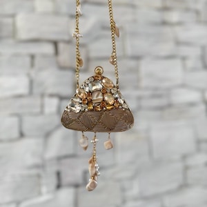 May include: A gold-coloured necklace with a triangular pendant embellished with clear and amber gemstones. The pendant has a wireframe design with a spiral pattern at the base. The necklace includes dangling pearl and stone accents.