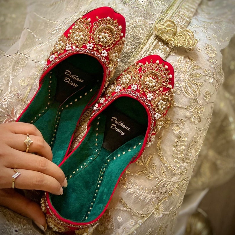 K&ouml;nnte beinhalten: Ein Paar rote Samtschuhe mit goldenen und perlmuttartigen Verzierungen. Die Schuhe haben ein gr&uuml;nes Innenfutter und der Text "Delhaus Diary" ist auf der Innensohle aufgedruckt.