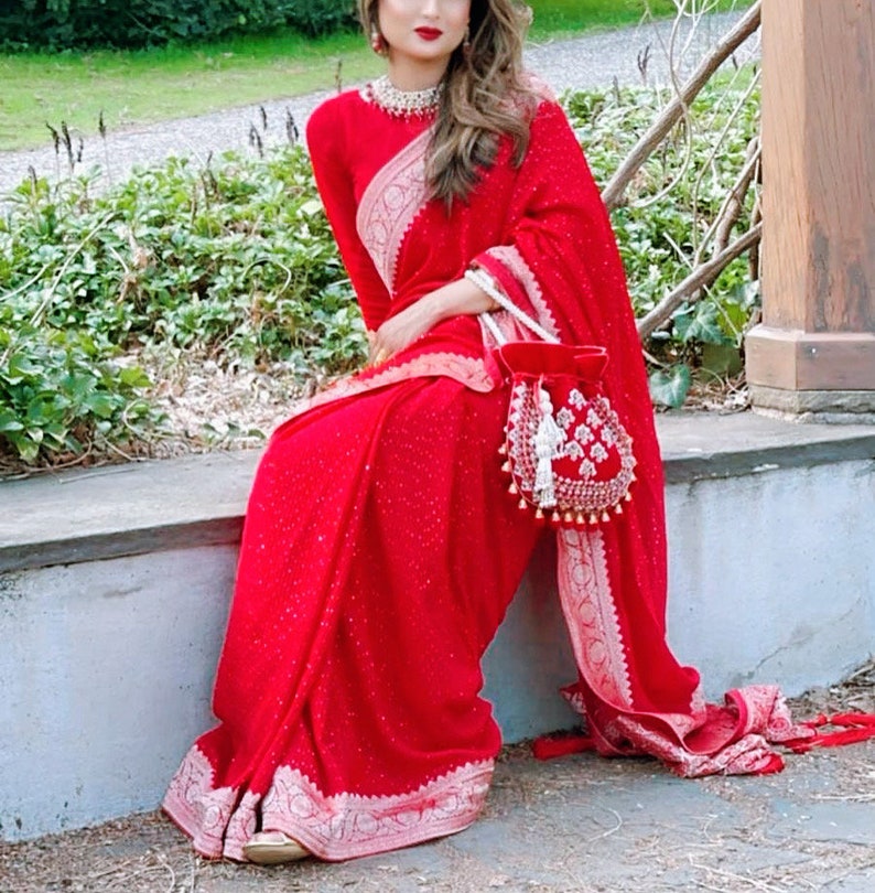 May include: A woman wearing a red saree with silver embroidery and a red beaded bag. The saree has a sparkly texture.