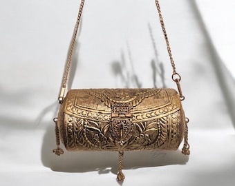May include: A gold metal clutch bag with an ornate floral design and a chain strap. The bag has a hinged clasp and a tassel.