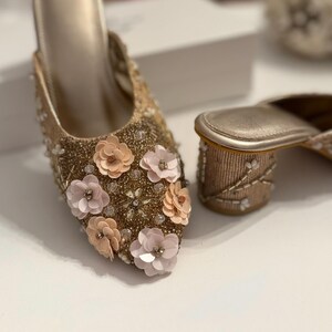 以下が含まれることがあります： ピンクとピーチの花のアクセントが付いた、ゴールドの装飾が施されたミュール2足