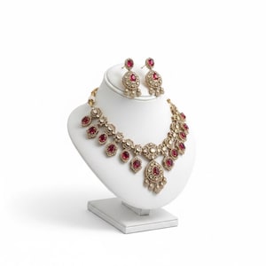 May include: A gold-toned necklace and matching earring set featuring oval-shaped red stones and clear crystals. The necklace has a central teardrop pendant with smaller dangling elements, while the earrings mirror the design with a single oval stone.