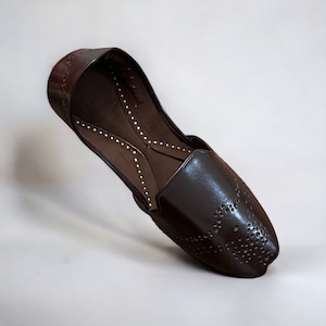 May include: A pair of brown leather shoes with a pointed toe and a decorative pattern of small holes. The shoes have a slip-on design and a flat sole.