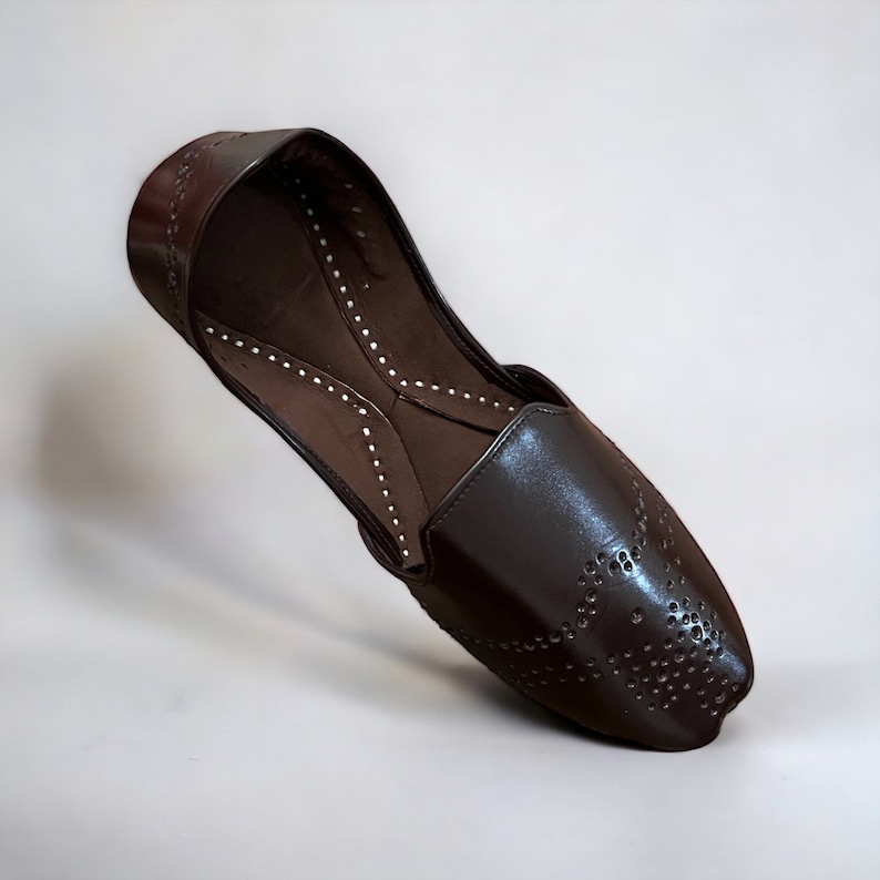 May include: A pair of brown leather shoes with a pointed toe and a decorative pattern of small holes. The shoes have a slip-on design and a flat sole.