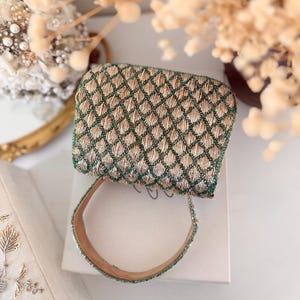 May include: A small, rectangular handbag with a woven pattern in gold and green. The bag has a matching handle and is resting on a white surface. The design features a diamond pattern, and the bag appears to be vintage or handmade.