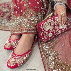 K&ouml;nnte beinhalten: Rote bestickte Brautschuhe mit Perlenbesatz und eine passende rote Samtclutch mit goldener Stickerei.