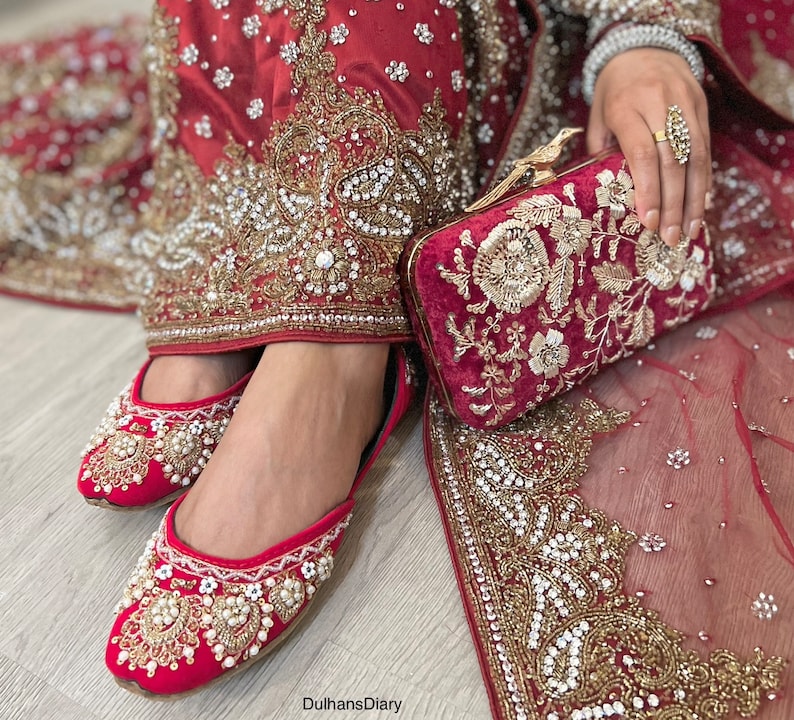 K&ouml;nnte beinhalten: Rote bestickte Brautschuhe mit Perlenbesatz und eine passende rote Samtclutch mit goldener Stickerei.