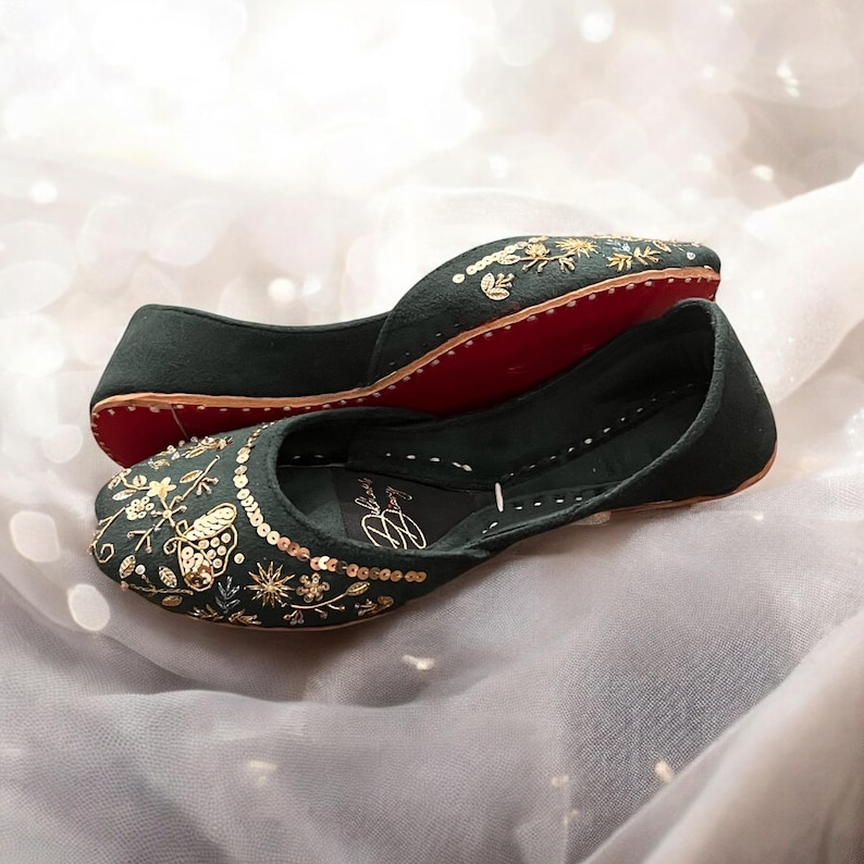 Pu&ograve; includere: Un paio di scarpe basse di colore verde scuro ricamate con filo dorato e paillettes. Le scarpe hanno un design a farfalla e una suola rossa.