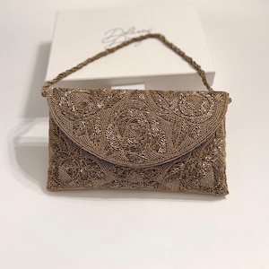 May include: A gold beaded clutch purse with a chain strap. The purse has a floral pattern and a flap closure.