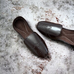 May include: A pair of brown leather shoes with decorative perforations. The shoes have a pointed toe and a slip-on design.