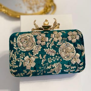 May include: A dark green velvet clutch with gold floral embroidery and a gold metal butterfly clasp.