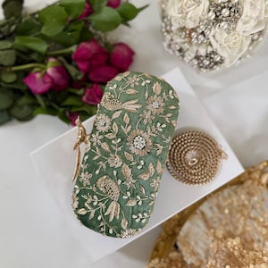 Op de afbeelding: Groene clutch met ingewikkelde bloemen- en vogelborduurwerk in gouddraad. De clutch heeft een goudkleurige handgreep en een afneembare gouden ketting. Het ontwerp bevat kleine witte kralen. Een stijlvol accessoire voor speciale gelegenheden.