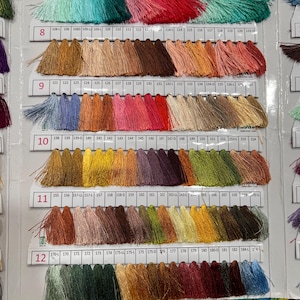 May include: A color chart of thread samples, featuring a wide array of hues. The chart displays numbered rows of thread bundles, ranging from vibrant greens and pinks to earthy browns and blues. The brand name "NEELAM THREAD PVT LTD." is visible.