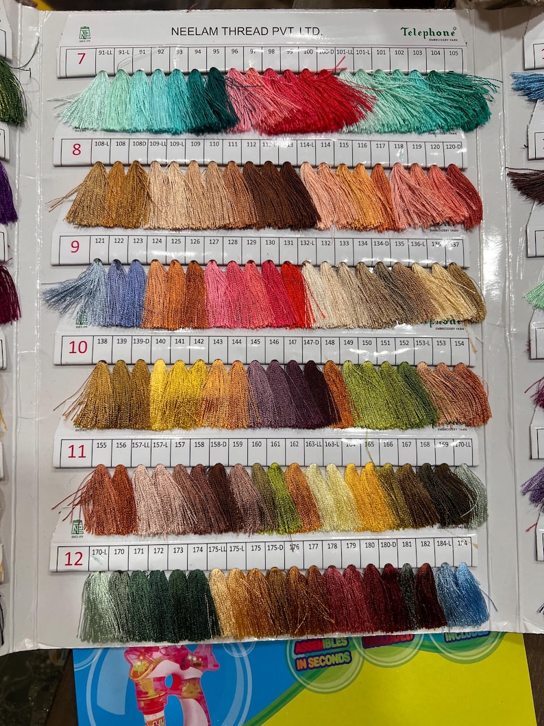 May include: A color chart of thread samples, featuring a wide array of hues. The chart displays numbered rows of thread bundles, ranging from vibrant greens and pinks to earthy browns and blues. The brand name "NEELAM THREAD PVT LTD." is visible.