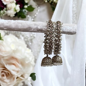 May include: A pair of gold earrings with pearl and clear rhinestone accents. The earrings have a bell-shaped design.